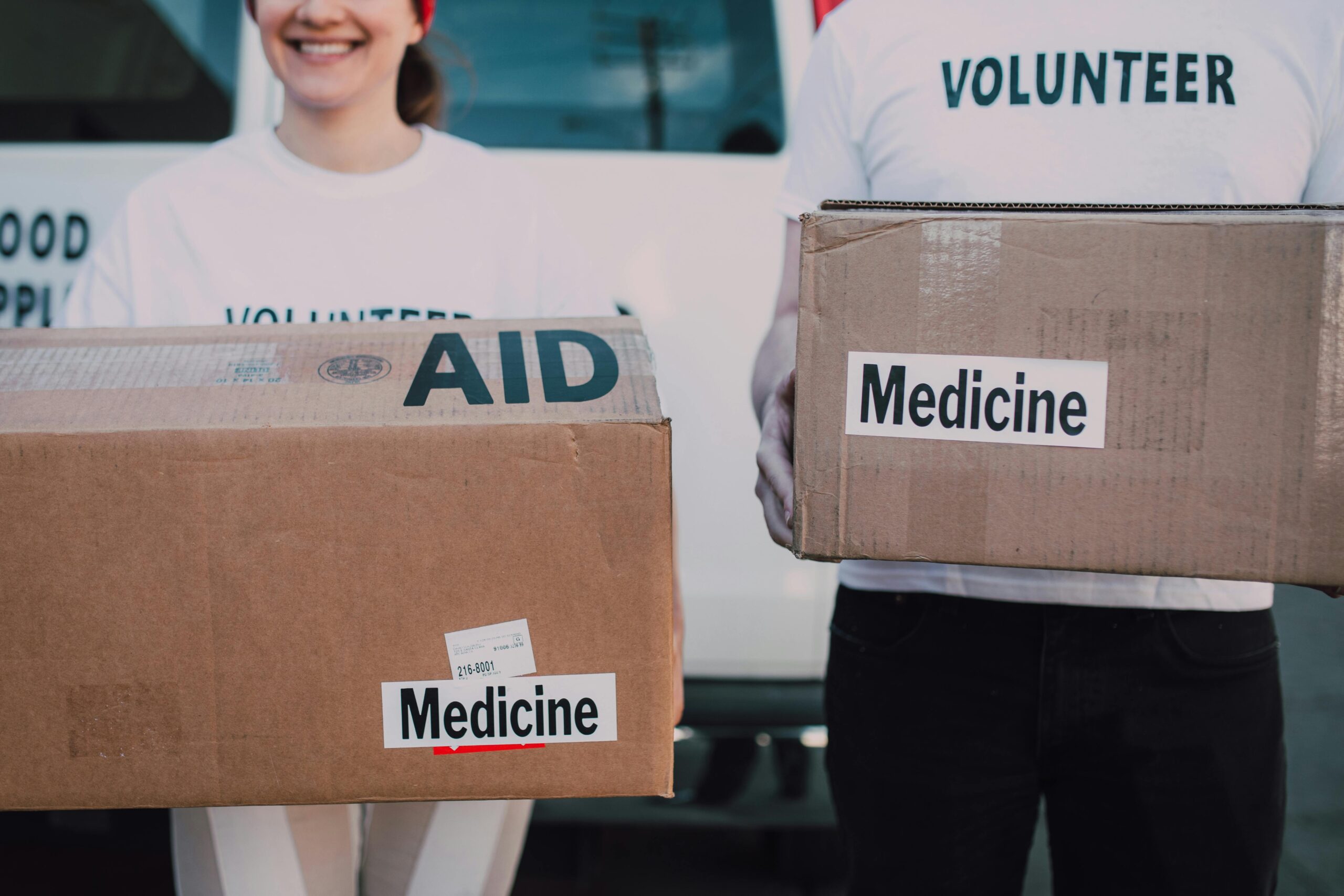 Volunteers holding boxes labeled 'AID' and 'Medicine', preparing donations.